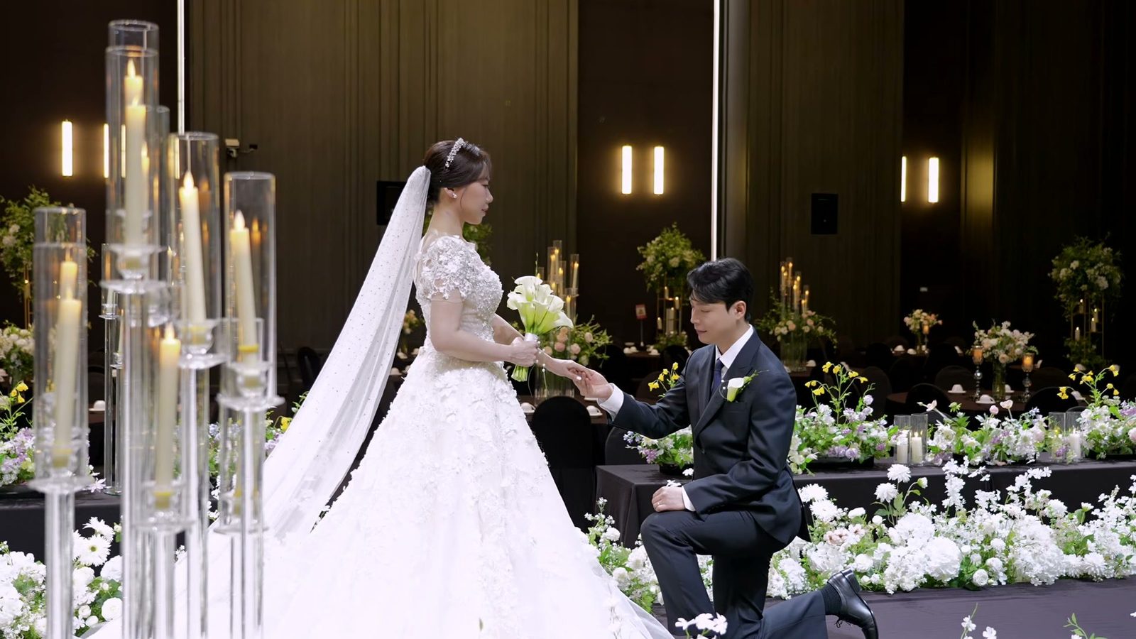 하객이 앉기 전 빈 홀의 버진로드에서 신랑이 한쪽 무릎을 꿇고 신부의 손을 잡은 모습