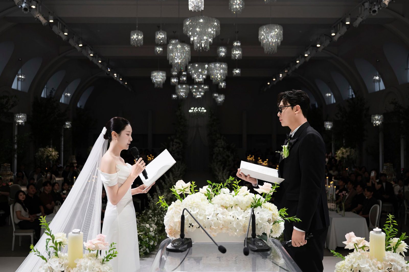 어두워진 홀 단상에서 마주 서서 마이크를 들고 서약문을 읽는 신부와 신랑